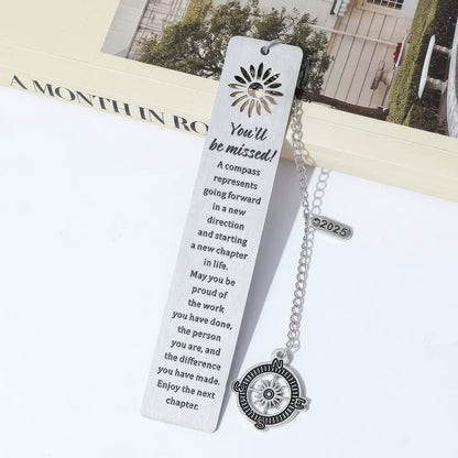 Compass metal bookmark with chain, placed in open book, light background