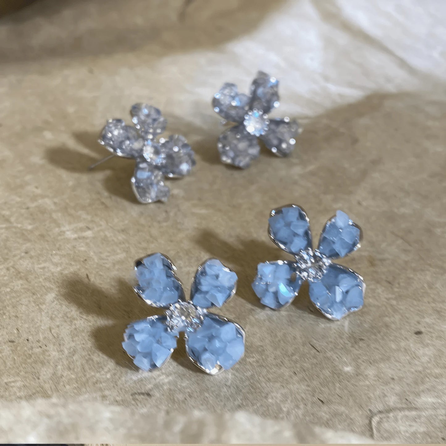 Crystal flower earrings, clear and blue, displayed on beige pad