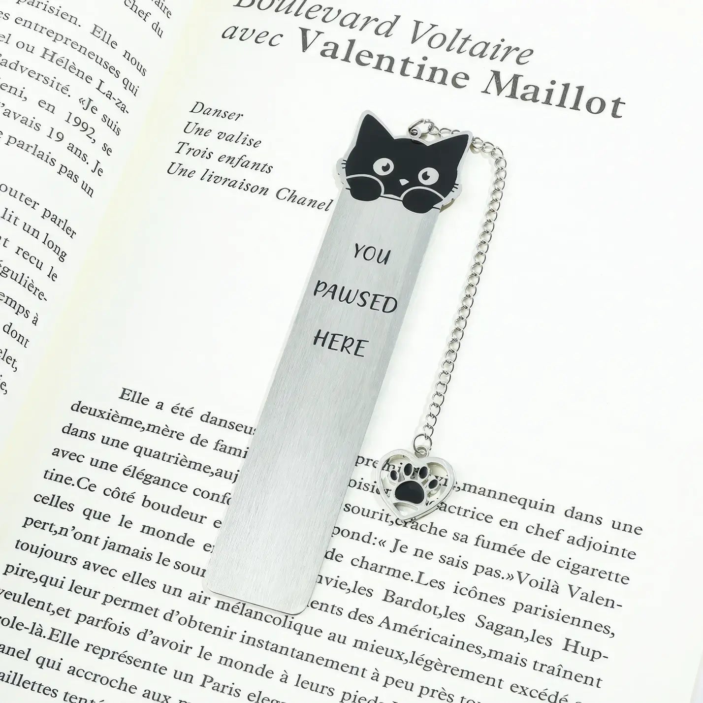 Cute cat stainless steel bookmark with chain and paw charm, placed in open book, white background