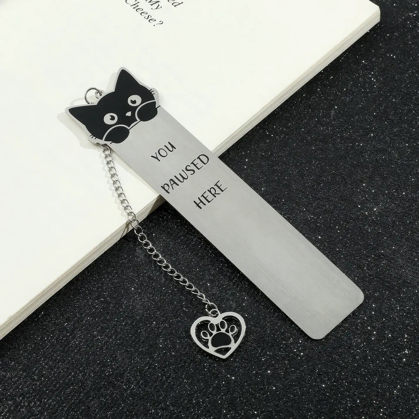 Cute cat stainless steel bookmark with chain and paw charm, displayed on black surface, white background