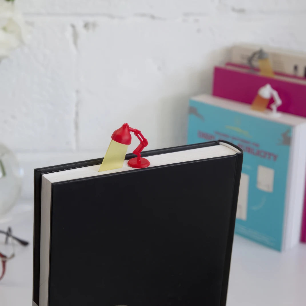 Red - and - yellow desk lamp - shaped bookmark clipped on black book, light background