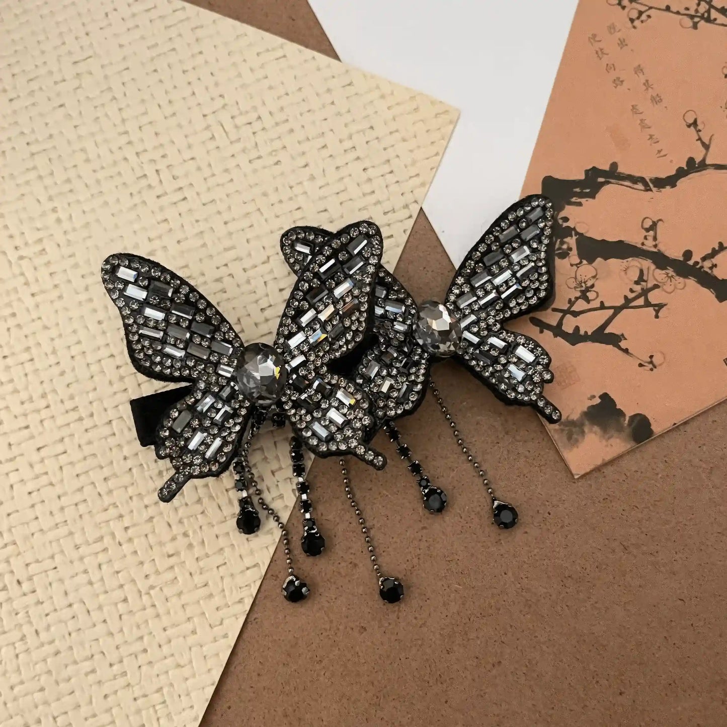 Black double butterfly tassel hair clip displayed on a textured surface with cards