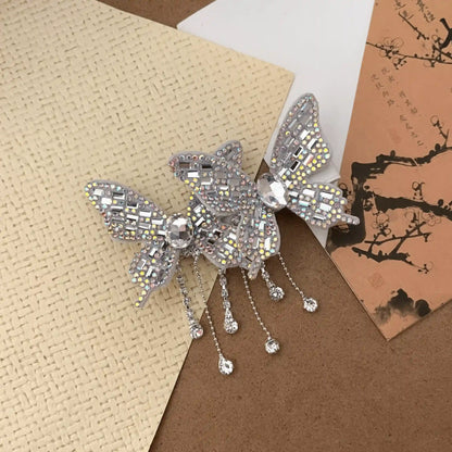Silver double butterfly tassel hair clip displayed on a textured surface with cards