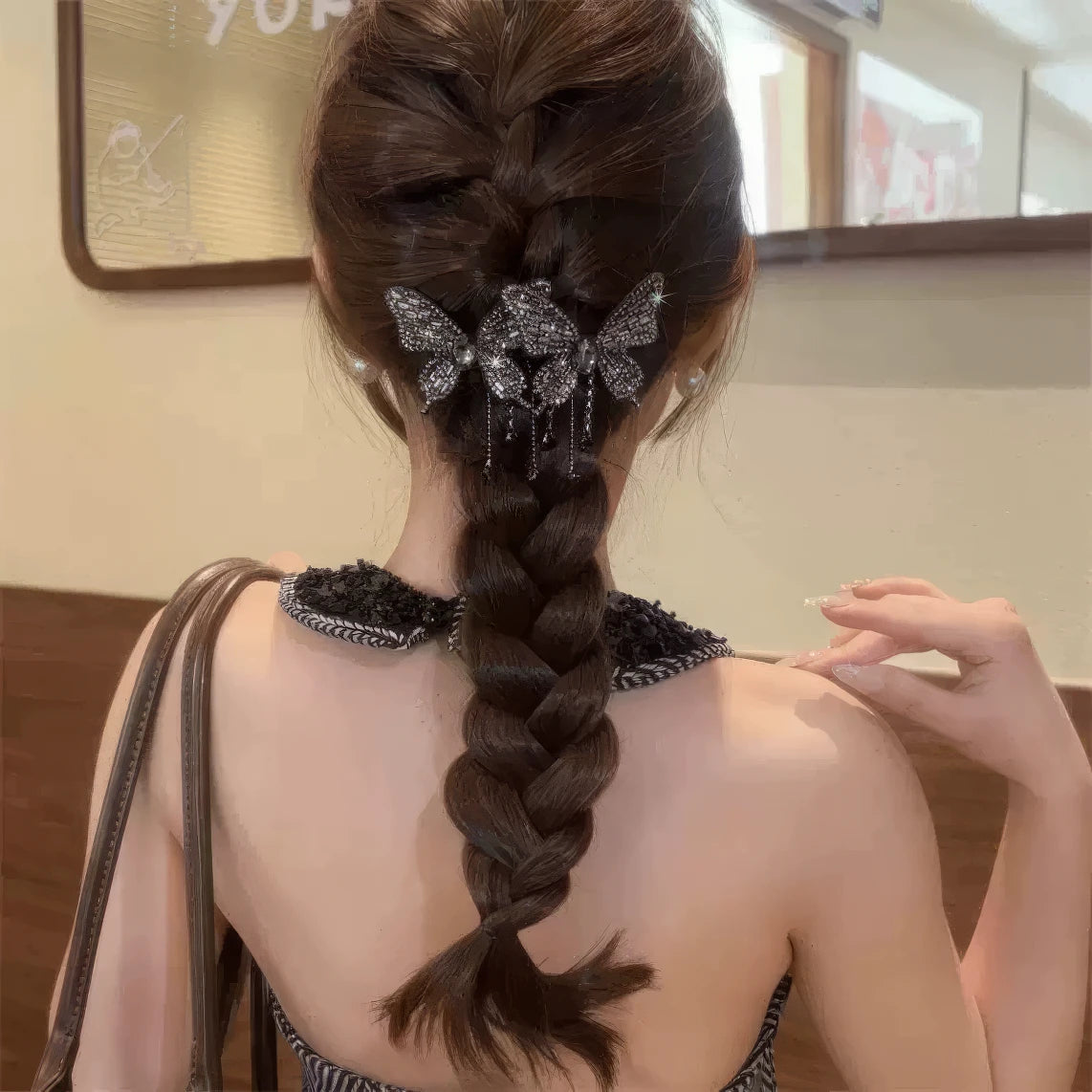 Black double butterfly tassel hair clip worn in a braided hairstyle, dark clothing background