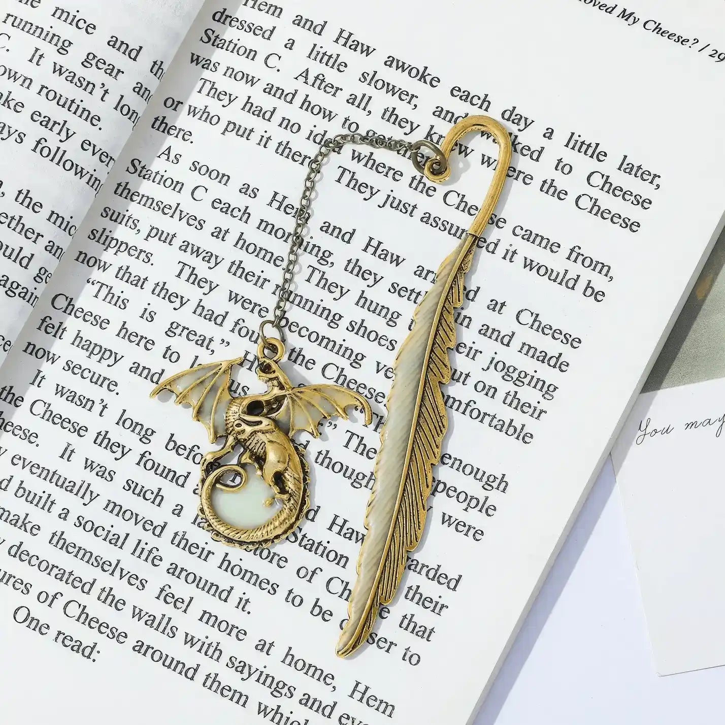 Feather four - winged dragon glow - in - the - dark bookmark placed in open book, light background