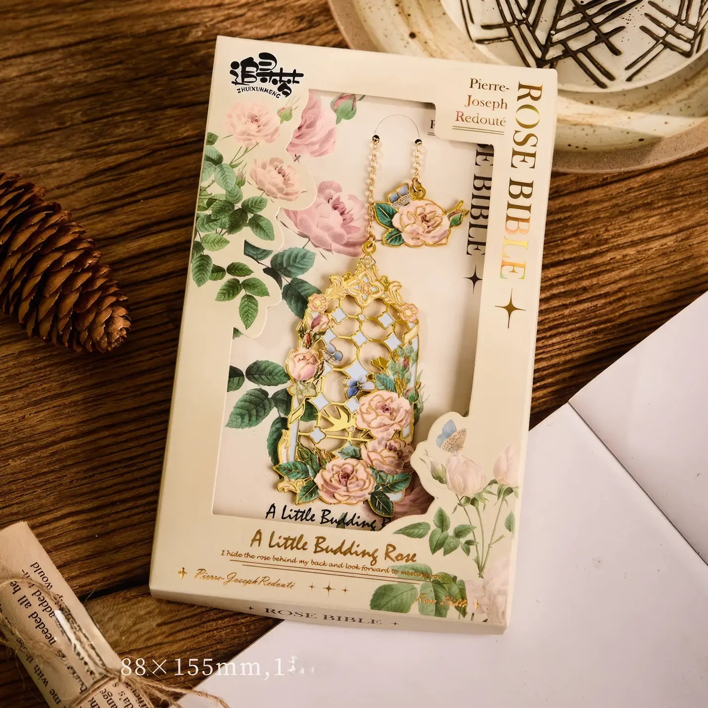 Floral story bookmark in beige package, displayed on wooden surface with stationery in background