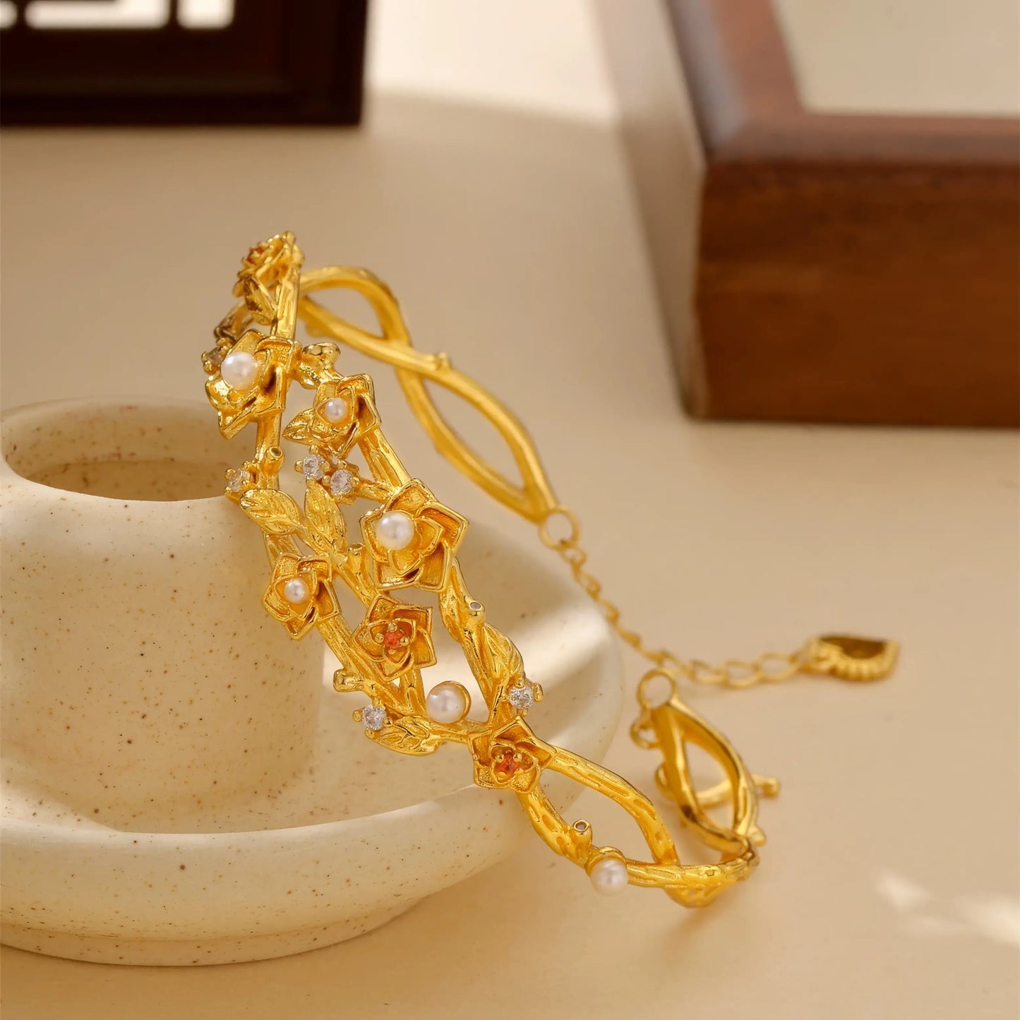 Side view of gold flower bracelet placed with cup, highlighting details