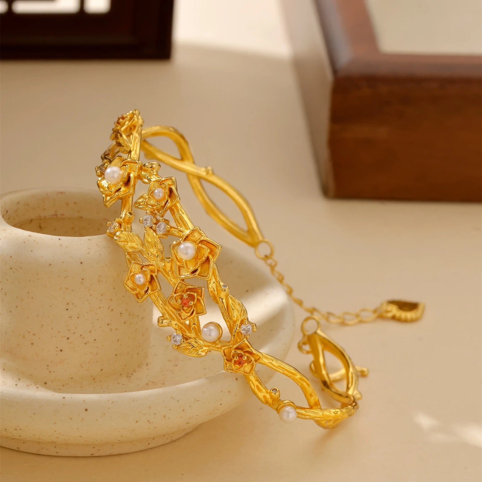 Side view of gold flower bracelet placed with cup, highlighting details