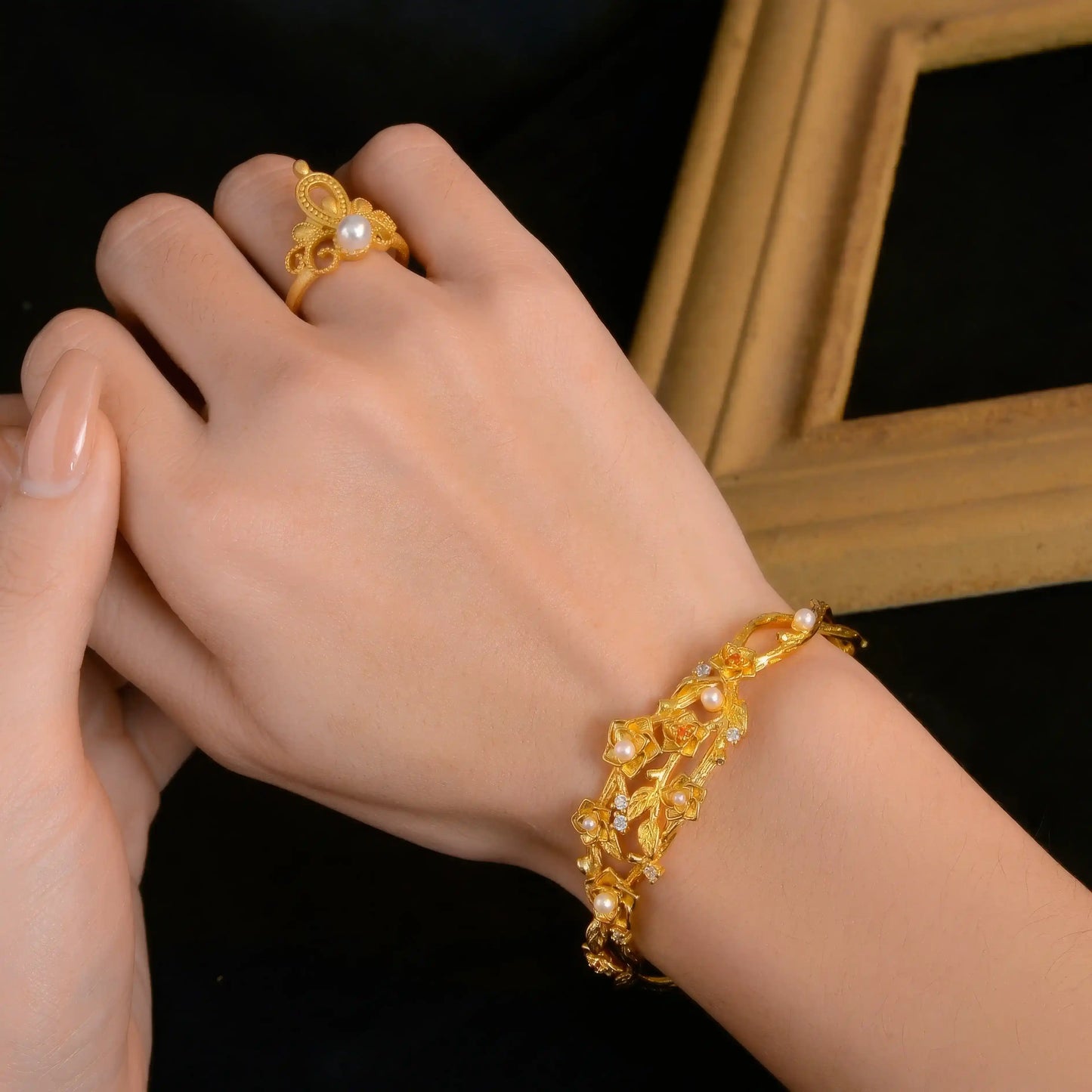 Gold flower bracelet worn on wrist, paired with ring, black background