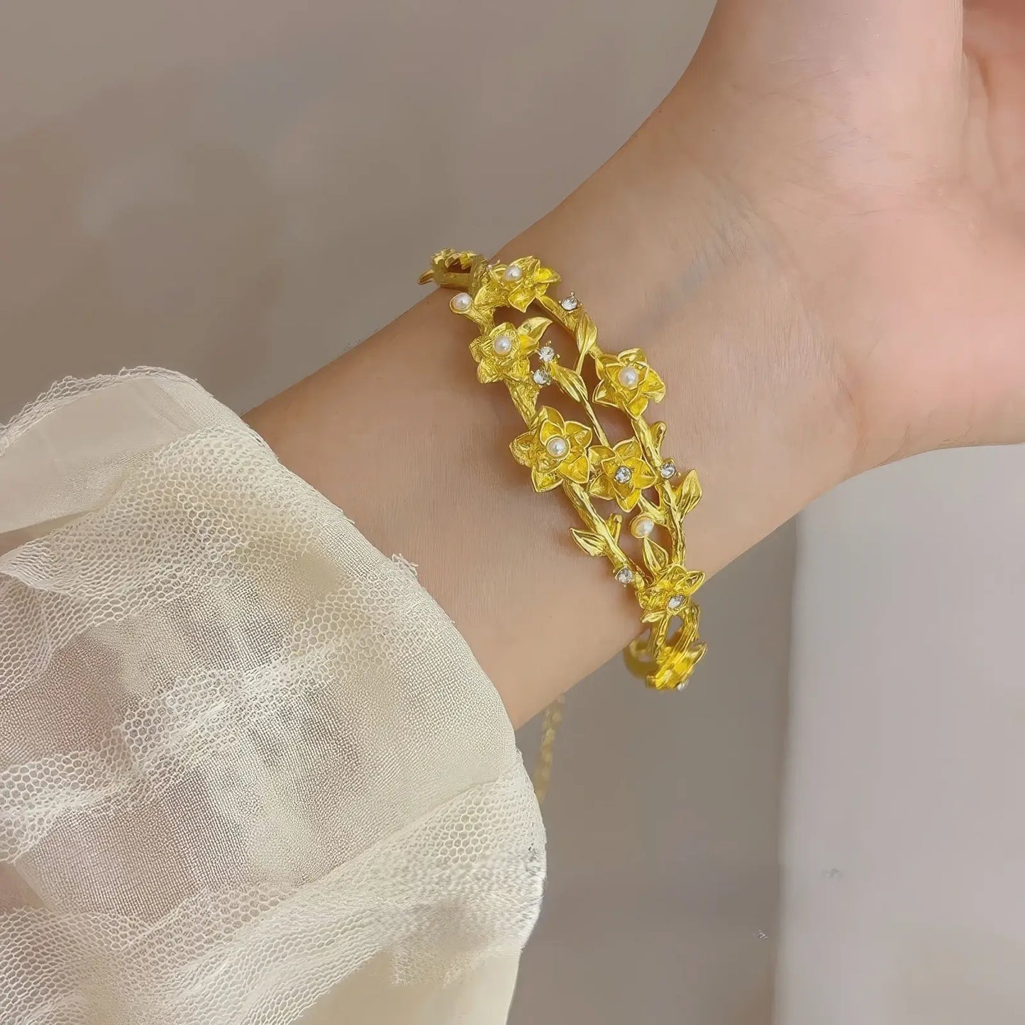 Gold flower bracelet worn on wrist, white lace sleeve in background