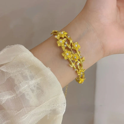 Gold flower bracelet worn on wrist, white lace sleeve in background