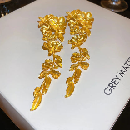 Gold flower leaf tassel earrings displayed on a “GREY MATTER” box