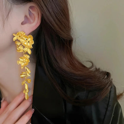 Gold flower leaf tassel earrings worn, black clothing background