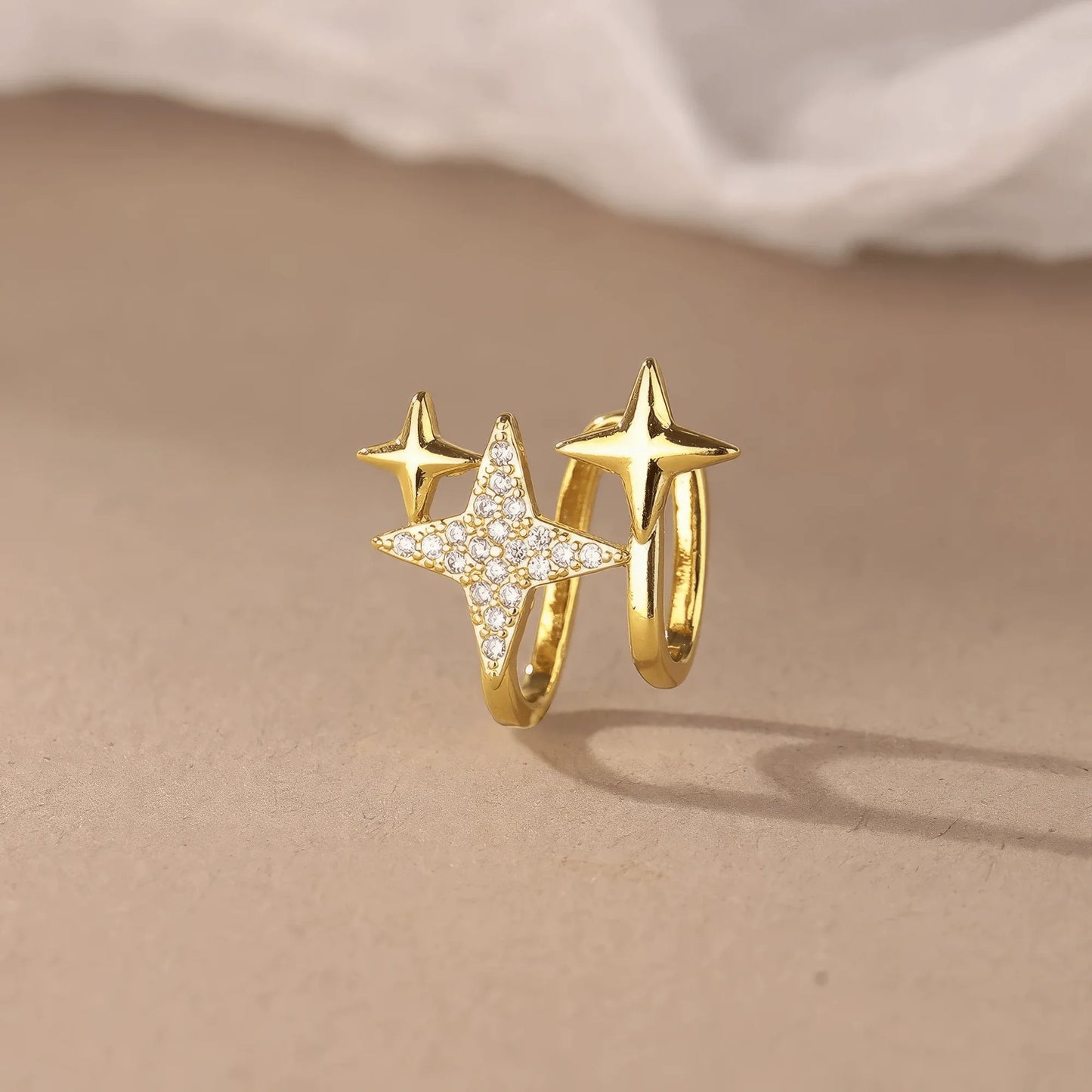Gold four - point star ear clip displayed on a beige surface, showcasing the elegant design