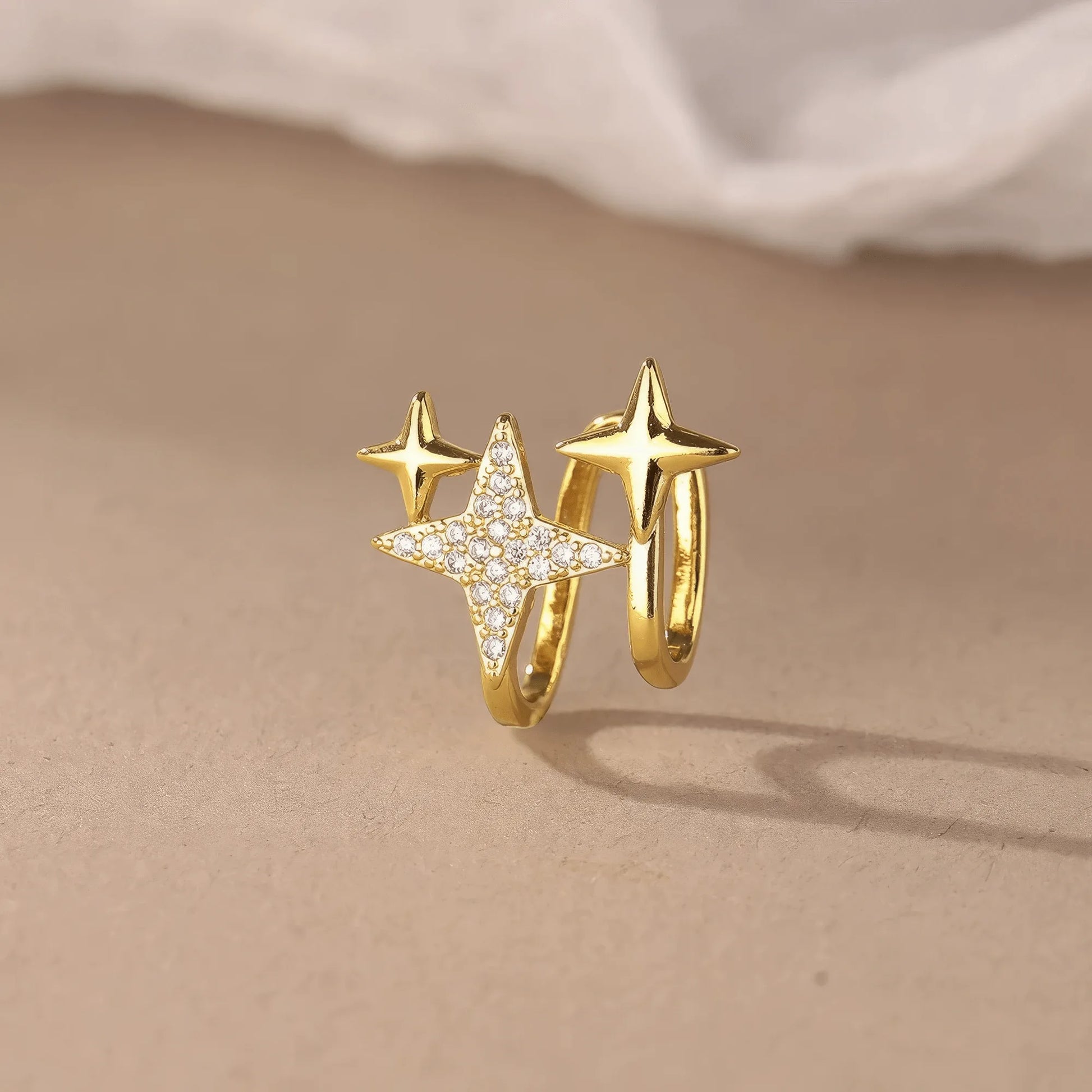Gold four - point star ear clip displayed on a beige surface, showcasing the elegant design