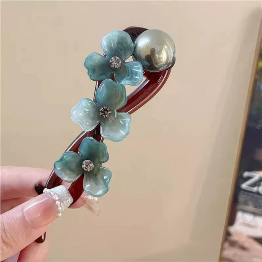 Hand holding French flower twist clip with blue flowers and pearl, light background