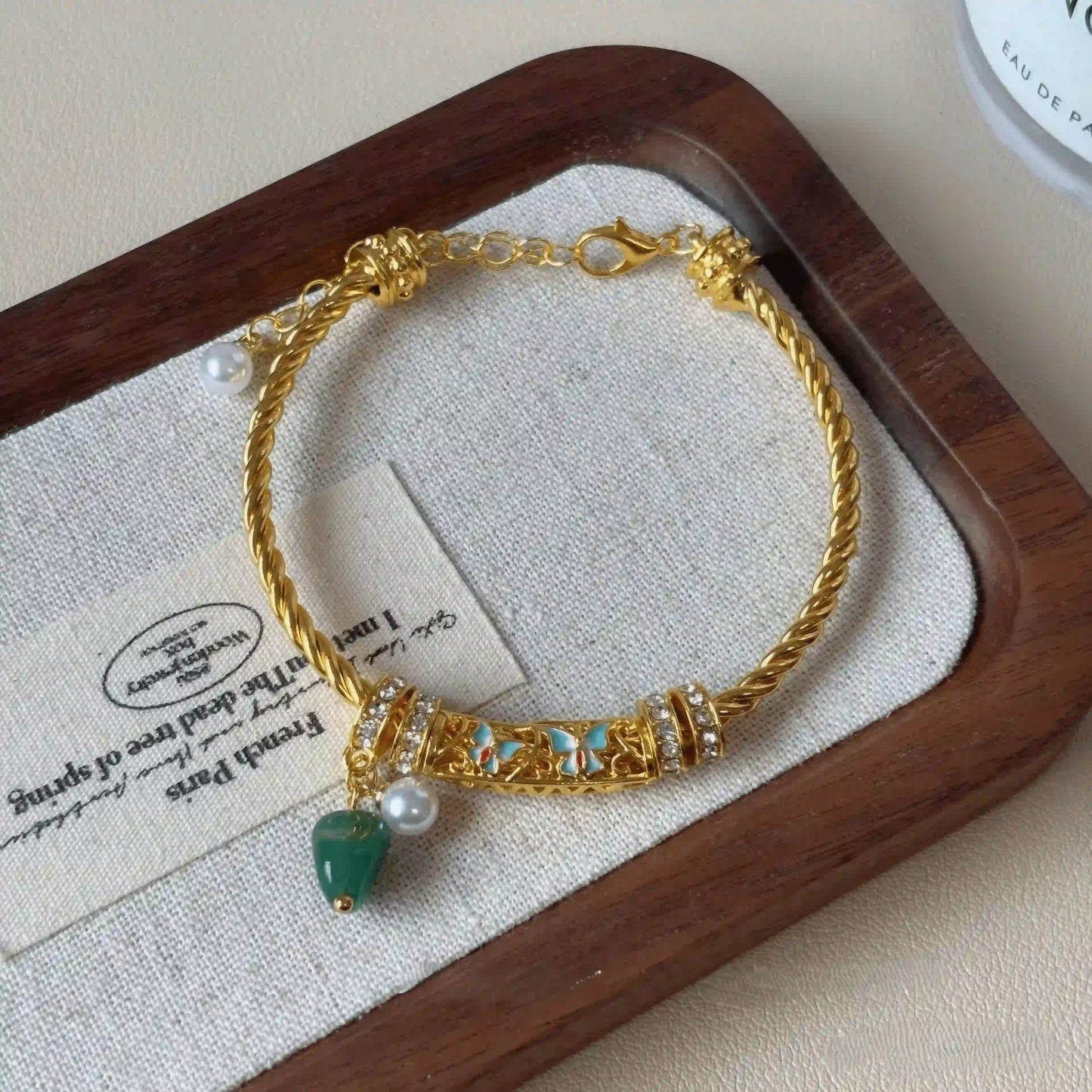 Glaze enamel twisted bracelet, gold - tone with green stone, displayed on beige pad with paper detail