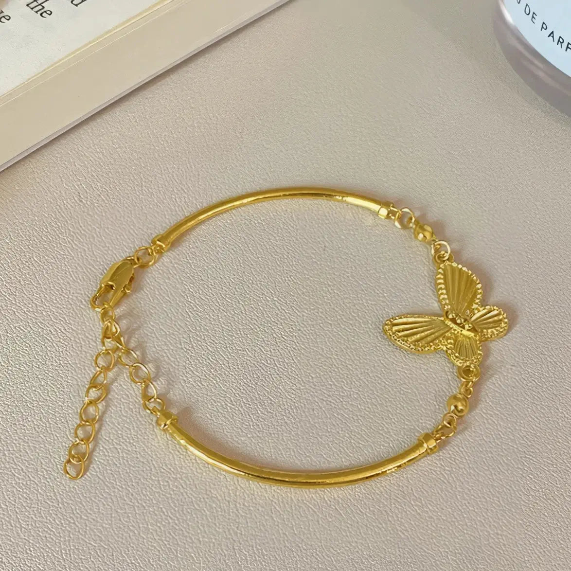 Gold butterfly bracelet displayed on a light surface, book in background