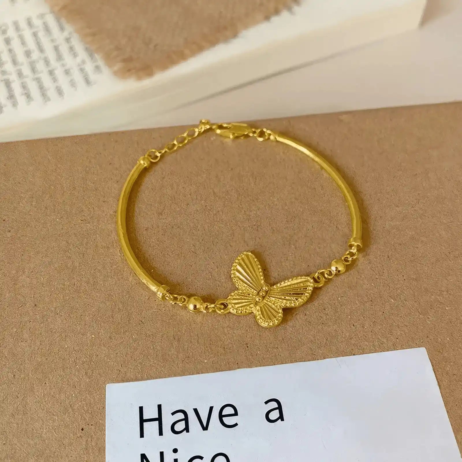 Gold butterfly bracelet displayed on a “Have a Nice” card, light surface