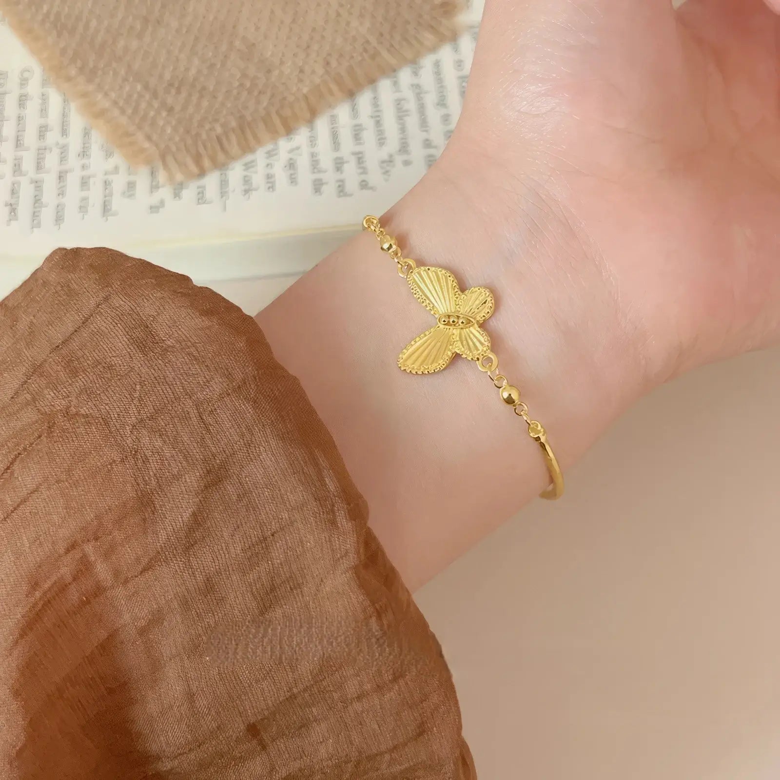 Gold butterfly bracelet worn on a wrist, brown sleeve background