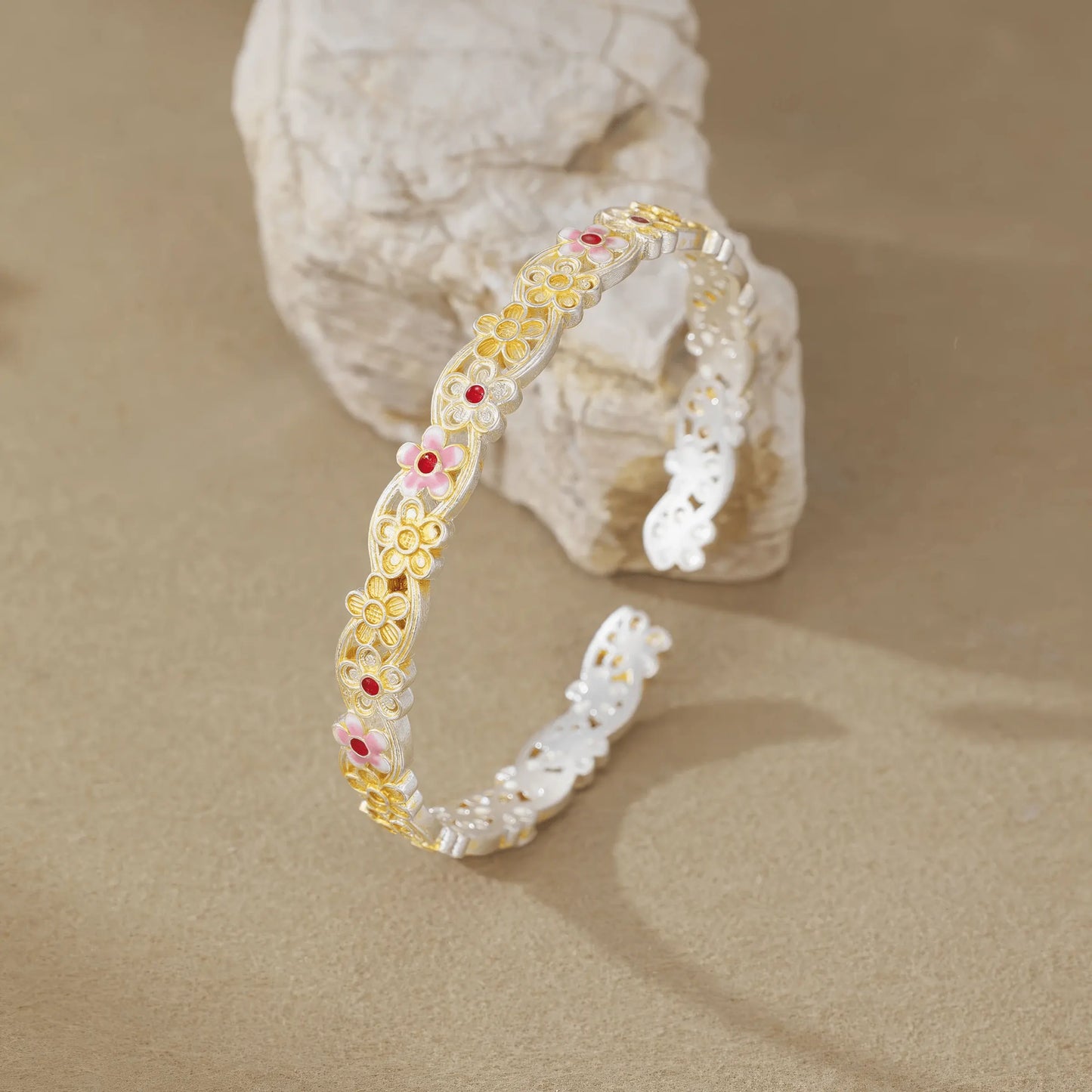 Gold - outlined flower bangle leaning on rock, emphasizing 3D structure
