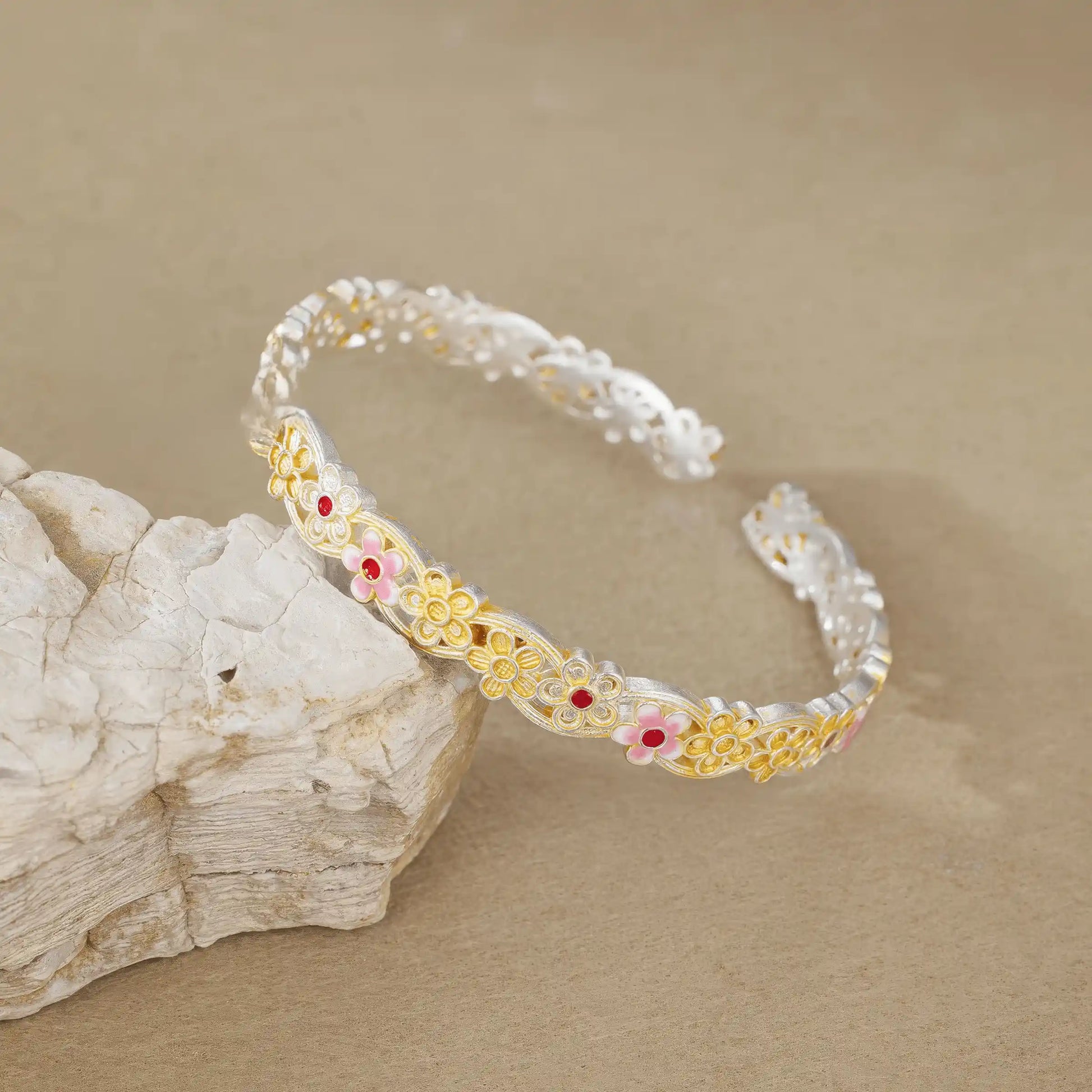 Gold - outlined flower bangle placed on rock, highlighting craftsmanship