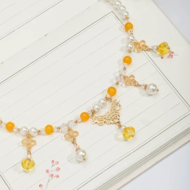 Gold - sprinkled pumpkin necklace with pearls and yellow beads, displayed on notebook, light background