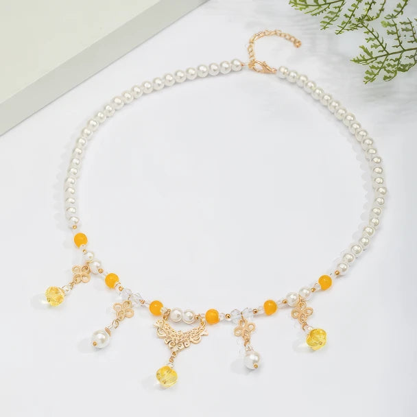 Gold - sprinkled pumpkin necklace with pearls and yellow beads, displayed on light surface, greenery in background