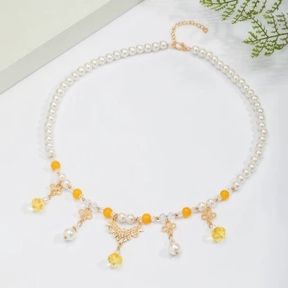 Gold - sprinkled pumpkin necklace with pearls and yellow beads, displayed on light surface, greenery in background