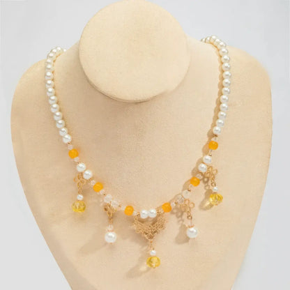 Gold - sprinkled pumpkin necklace with pearls and yellow beads, displayed on mannequin, light background