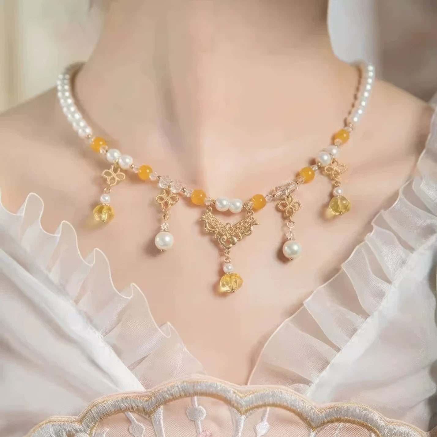 Woman wearing gold - sprinkled pumpkin necklace with pearls and yellow beads, white clothing background