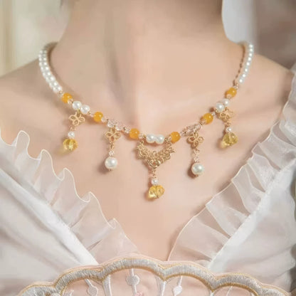 Woman wearing gold - sprinkled pumpkin necklace with pearls and yellow beads, white clothing background