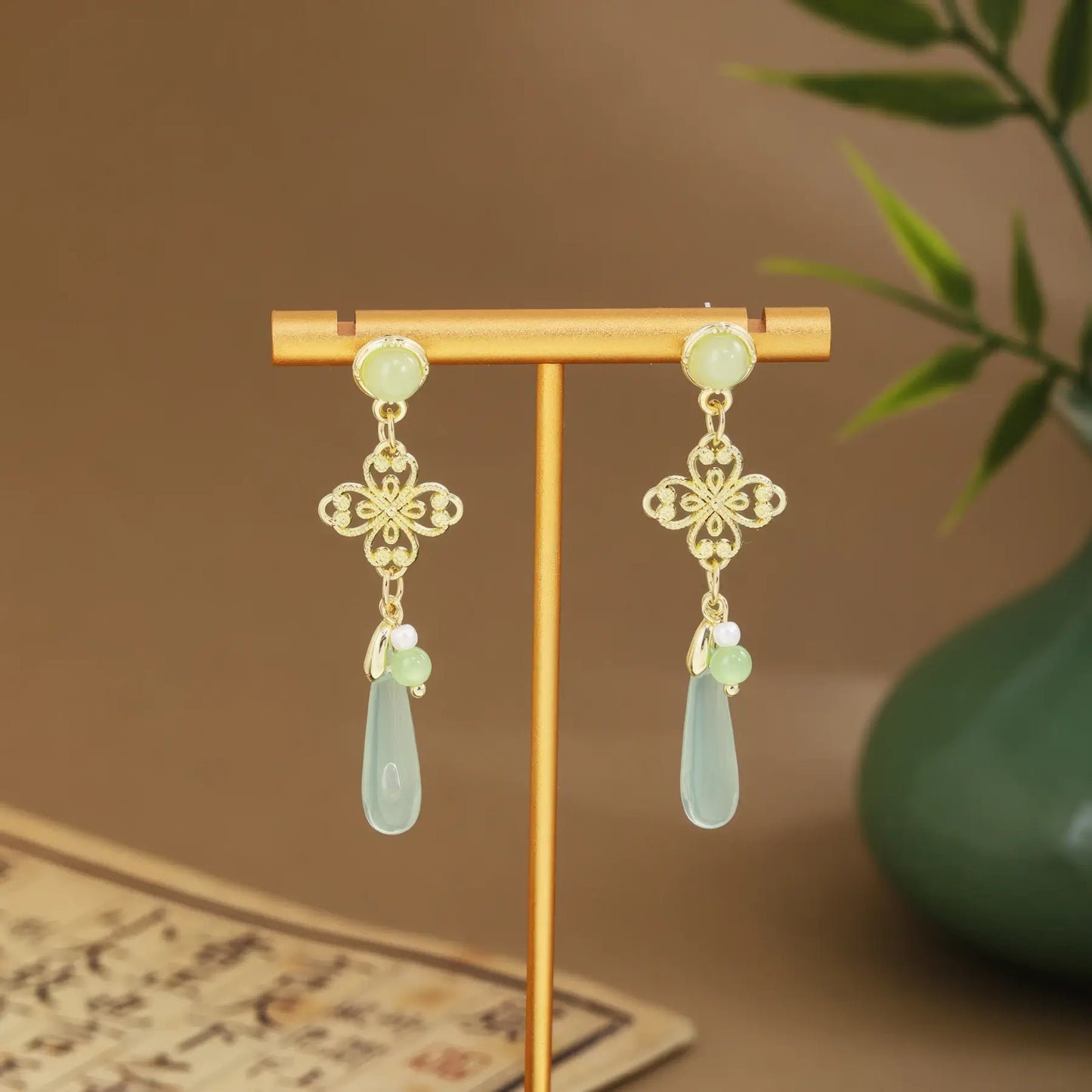 Green fan and bamboo tassel earrings on gold hanger, green vase background