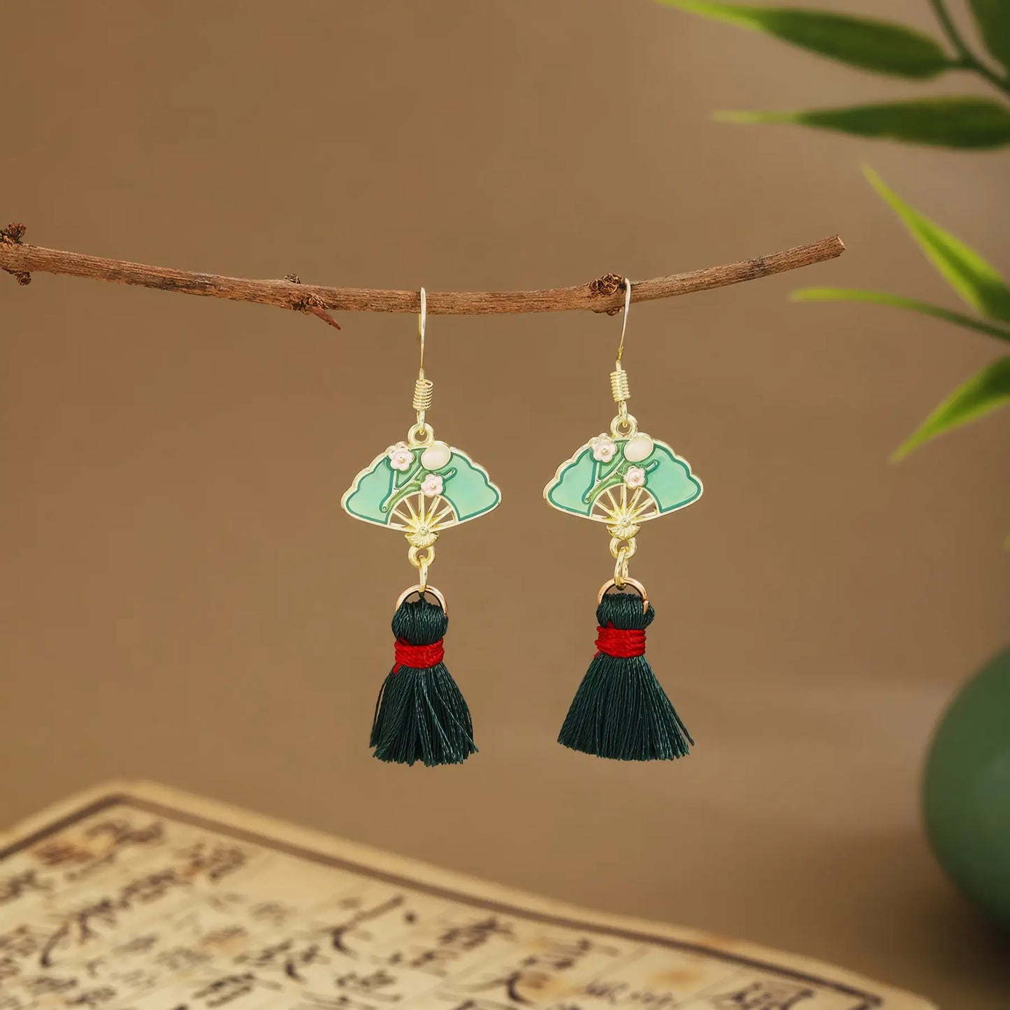 Fan earrings with black tassels and light green drops on wooden hanger, green vase and scroll