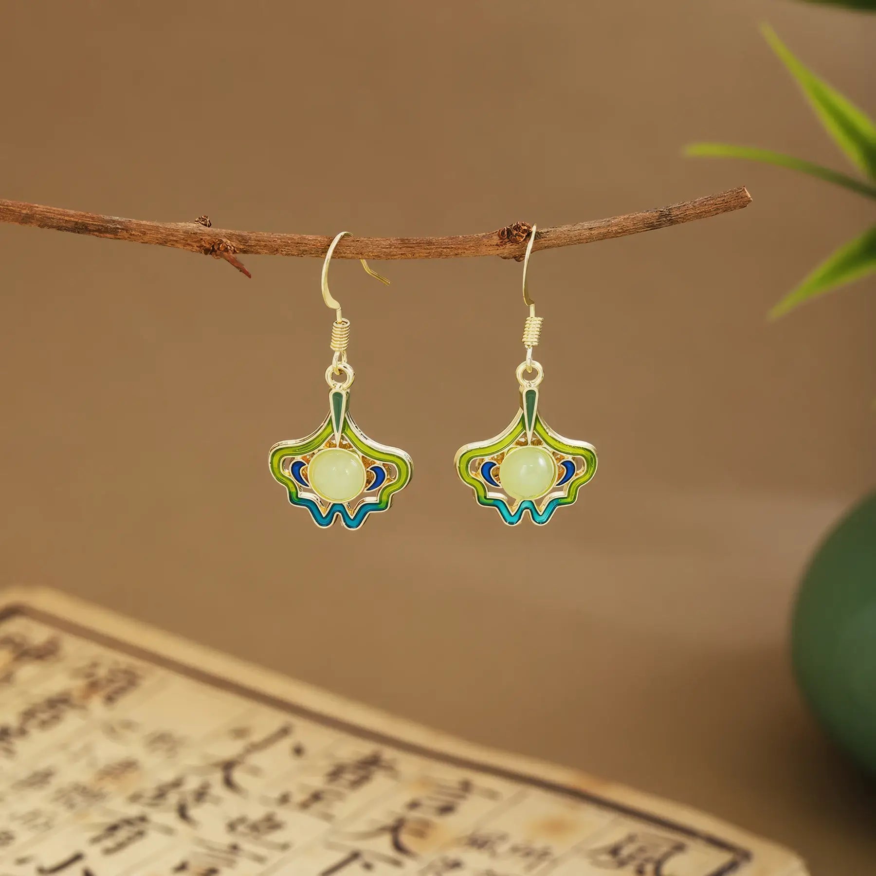 Colorful fan earrings with light green drops on wooden hanger, green vase and scroll