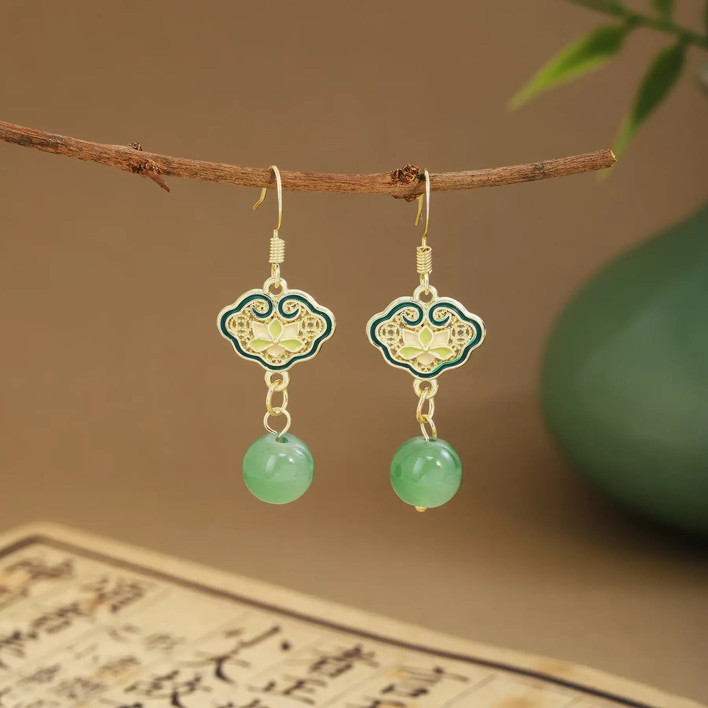Green fan tassel earrings on wooden hanger, green vase and scroll background