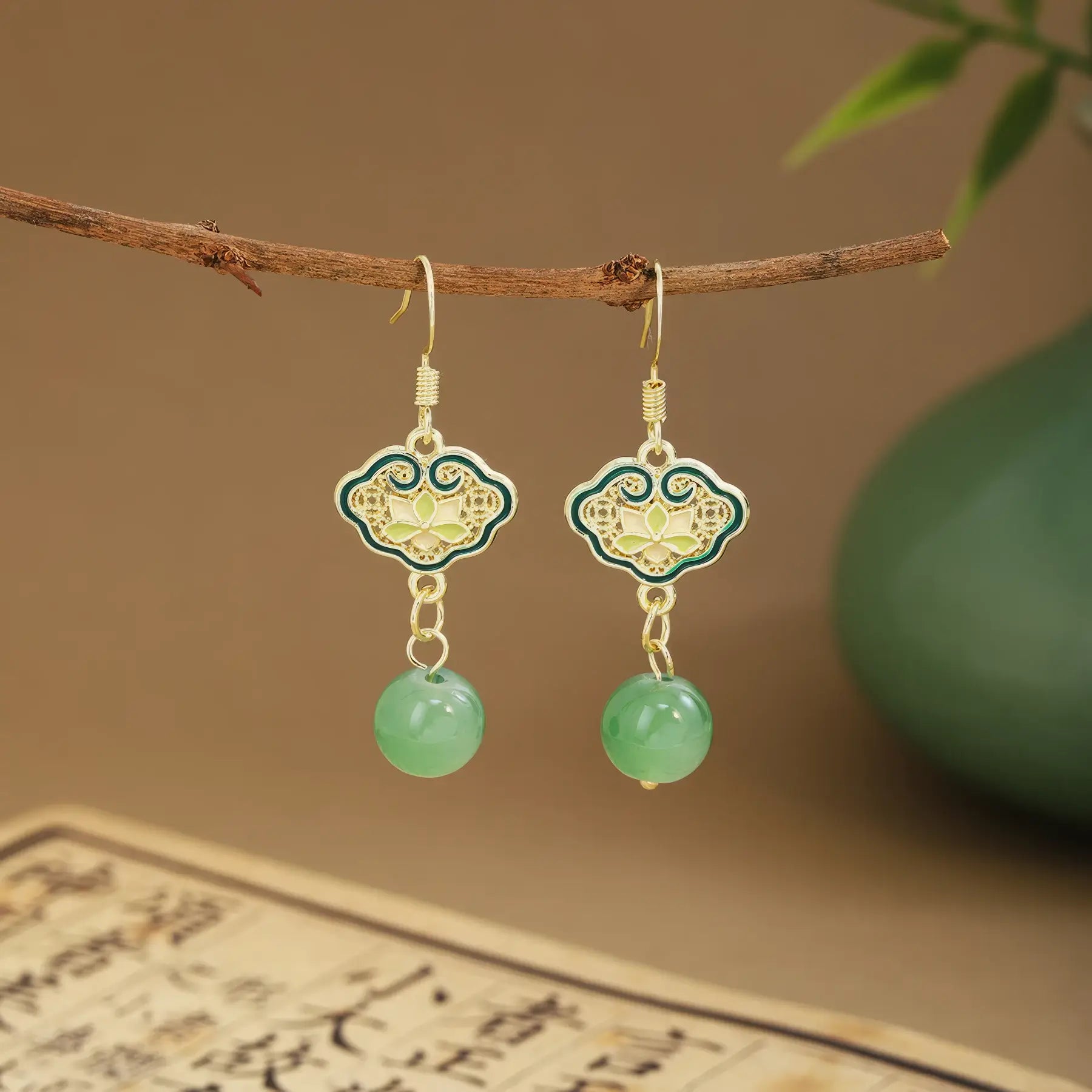 Green fan tassel earrings on wooden hanger, green vase and scroll background