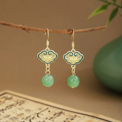Green fan tassel earrings on wooden hanger, green vase and scroll background