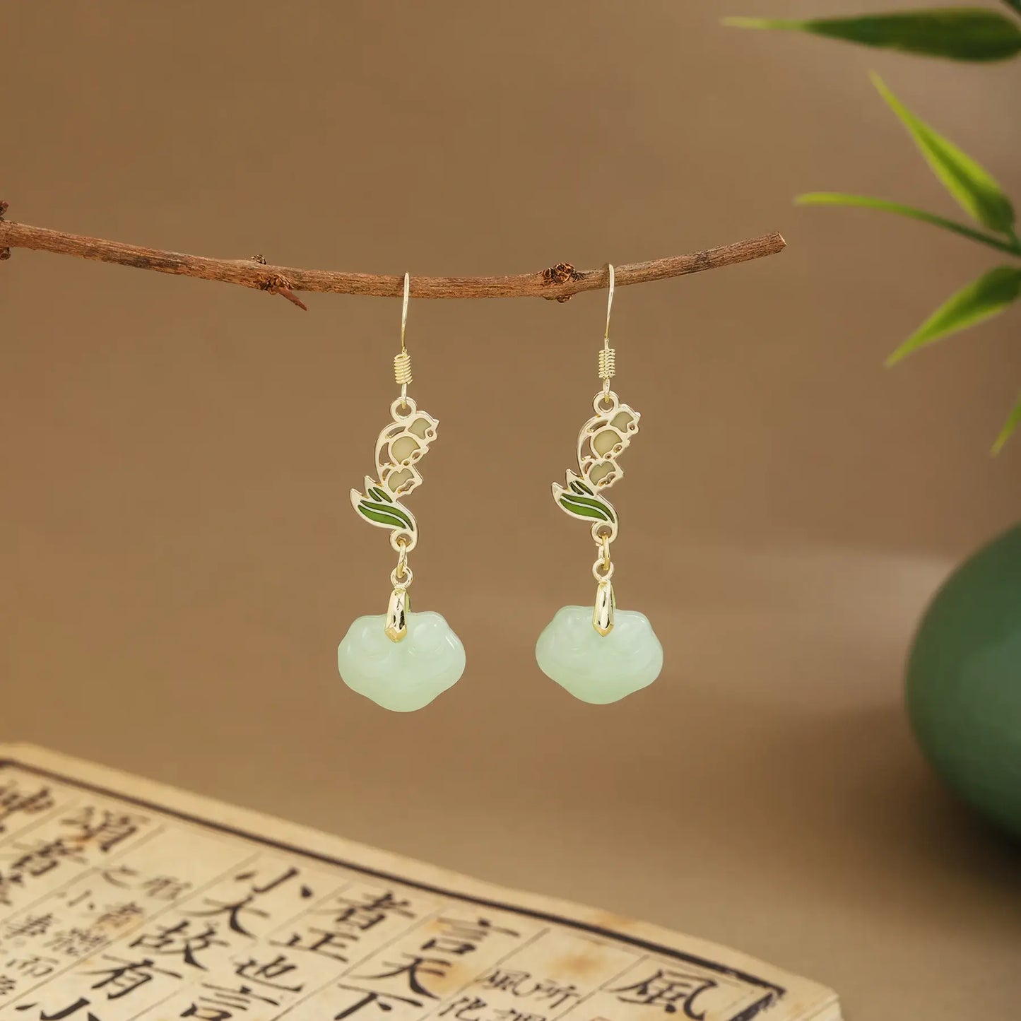 Green fan earrings with light green drops on wooden hanger, green vase and scroll