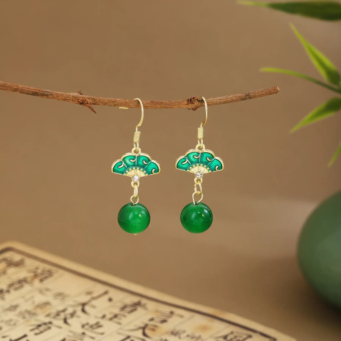 Green fan earrings with dark green drops on wooden hanger, green vase and scroll
