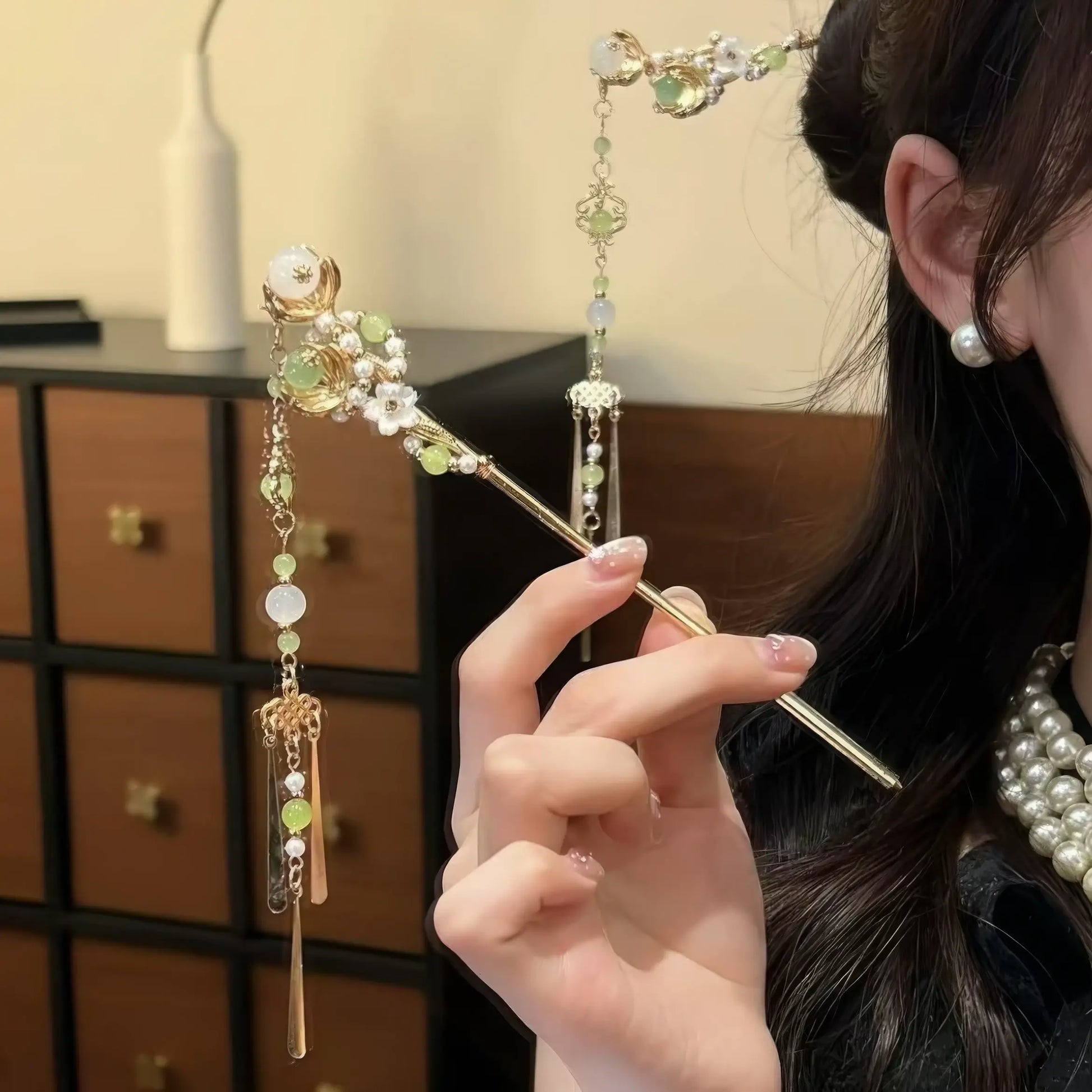 Green and gold tassel hairpin held by a model, showing the full length and dangling tassel details.