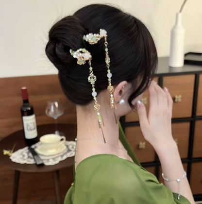 Green and gold tassel hairpin worn in a side bun, showing the side profile and tassel placement.