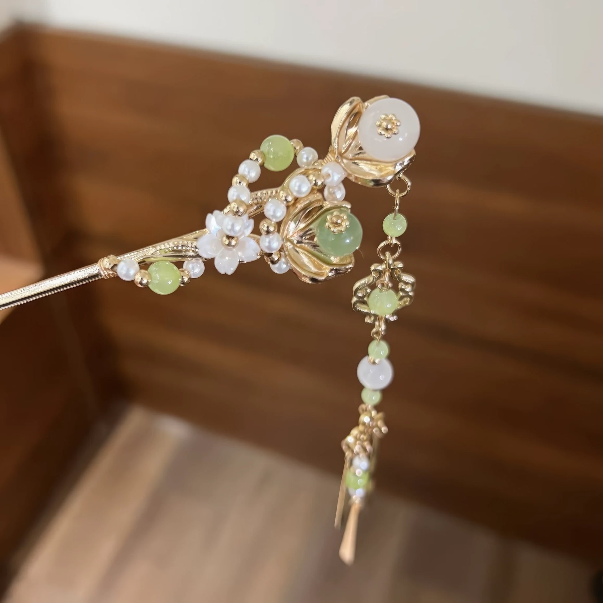 Close-up of a green jade and gold hairpin with pearls, flowers, and a hanging tassel.