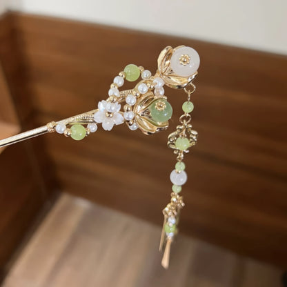Close-up of a green jade and gold hairpin with pearls, flowers, and a hanging tassel.
