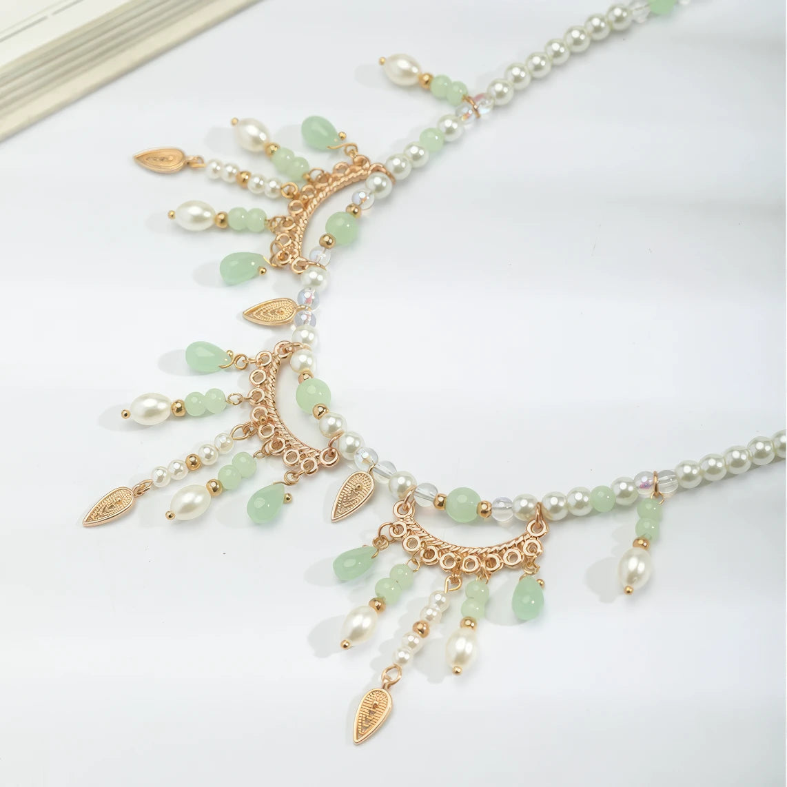 Detail of green multi - hole necklace with pearls and gold details, displayed on light surface, side view