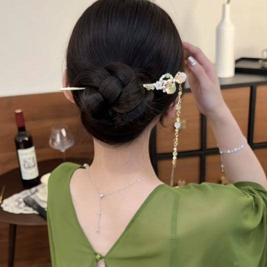 Back view of a low bun hairstyle with a green and gold tassel hairpin, showing the hanging tassel.