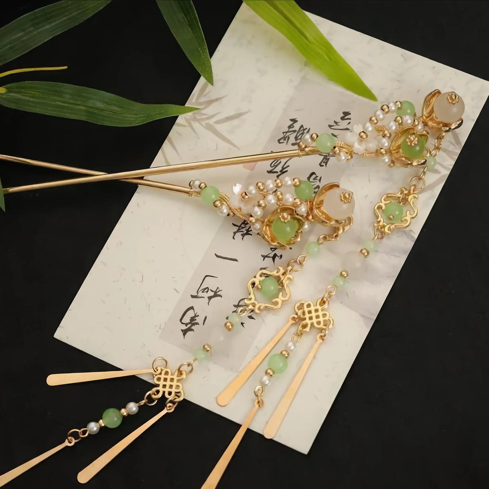 Green and gold hairpins with tassels arranged on traditional calligraphy paper with bamboo leaves.

