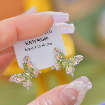 Hand holding green zircon butterfly earrings with a price tag
