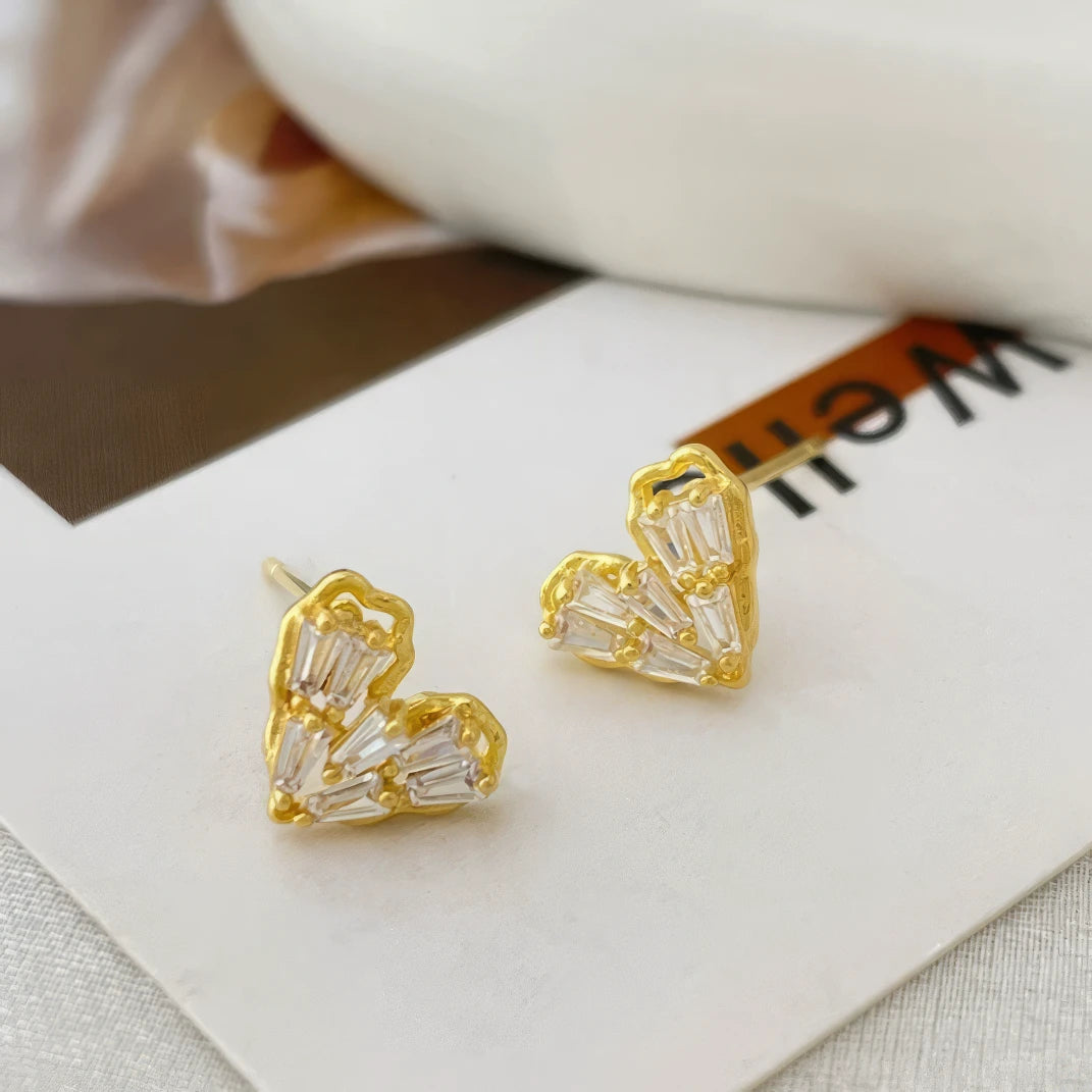 Gold - framed heart - shaped earrings placed on white card, highlighting design