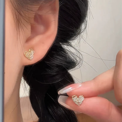 Small heart - shaped earrings worn on ear, hand adjusting, showcasing delicacy